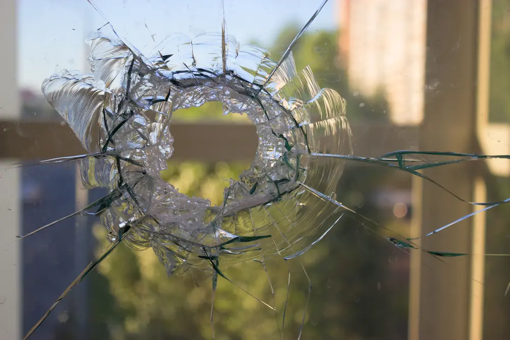 Großes Einschlagloch mit Rissen in einer Fensterscheibe vor unscharfem Hintergrund