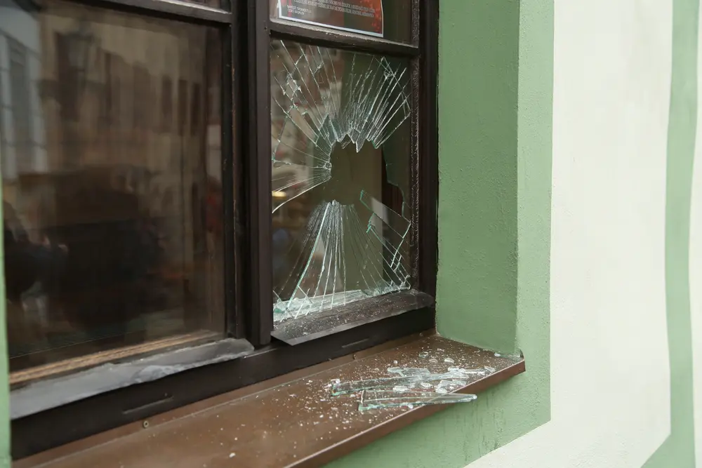 Eingeschlagene Fensterscheibe mit zerbrochenem Glas auf dem Fensterbrett eines Hauses